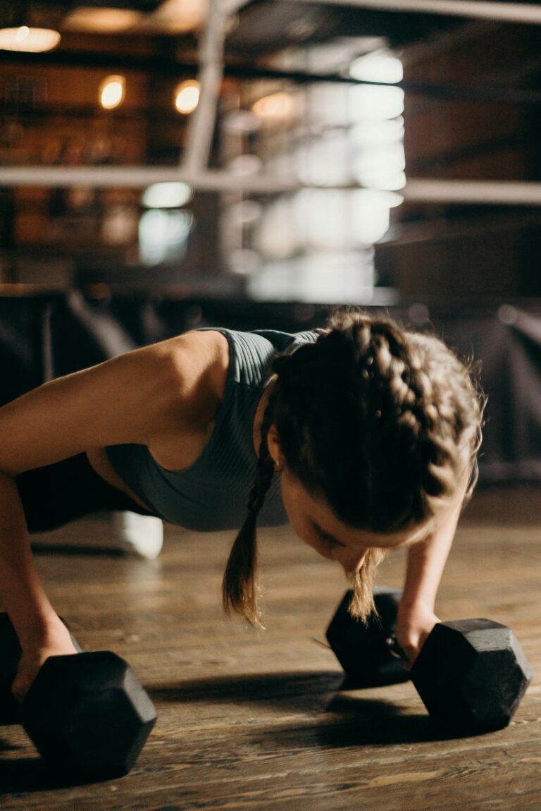 Fit woman doing push-ups with dumbbells indoors, emphasizing strength training and fitness.